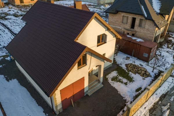 Aerial view of new residential house cottage and attached garage with shingle roof on fenced yard on sunny winter day in modern suburban area. Perfect investment in dream house.